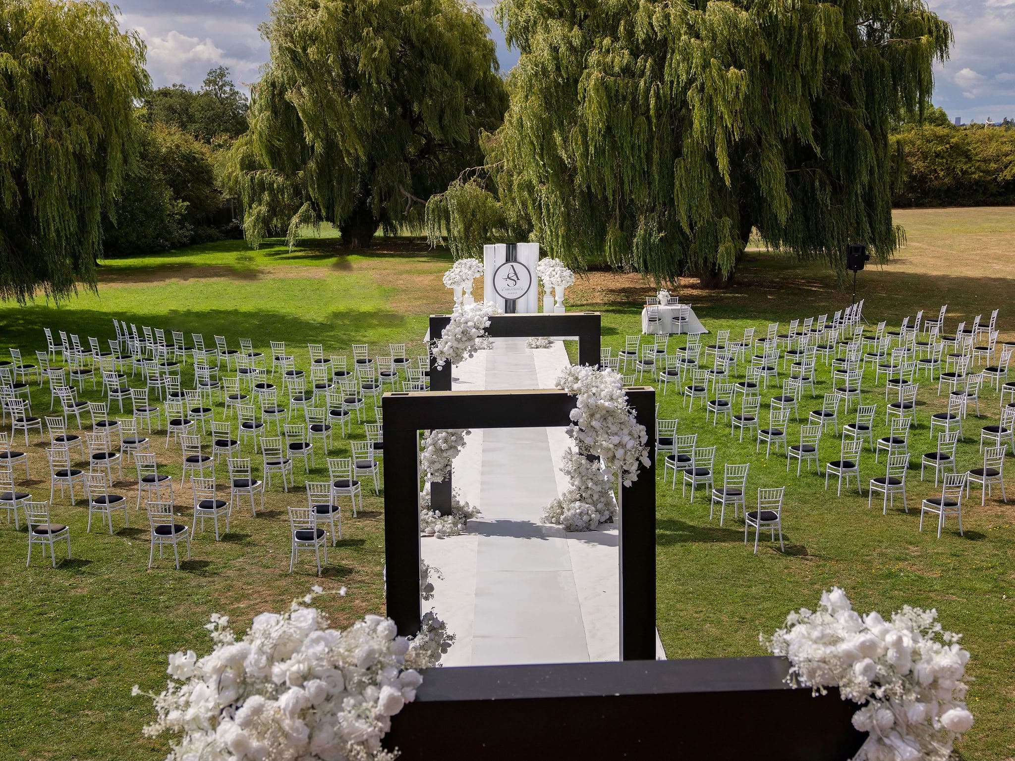 Outdoor ceremony with white chairs and a black and white floral aisle