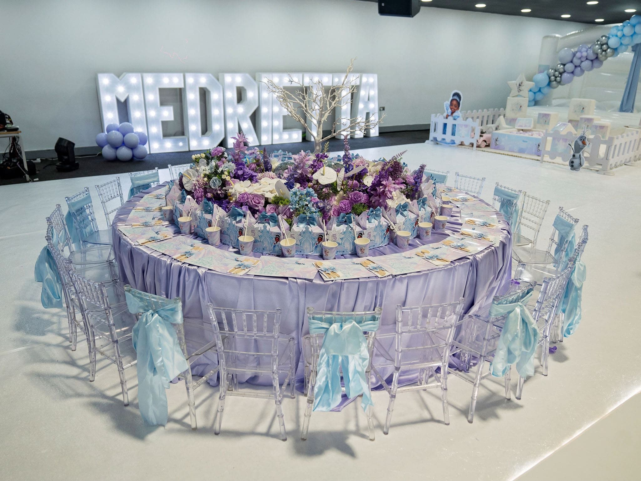 Circular children's party table with lilac flowers and blue ribbons