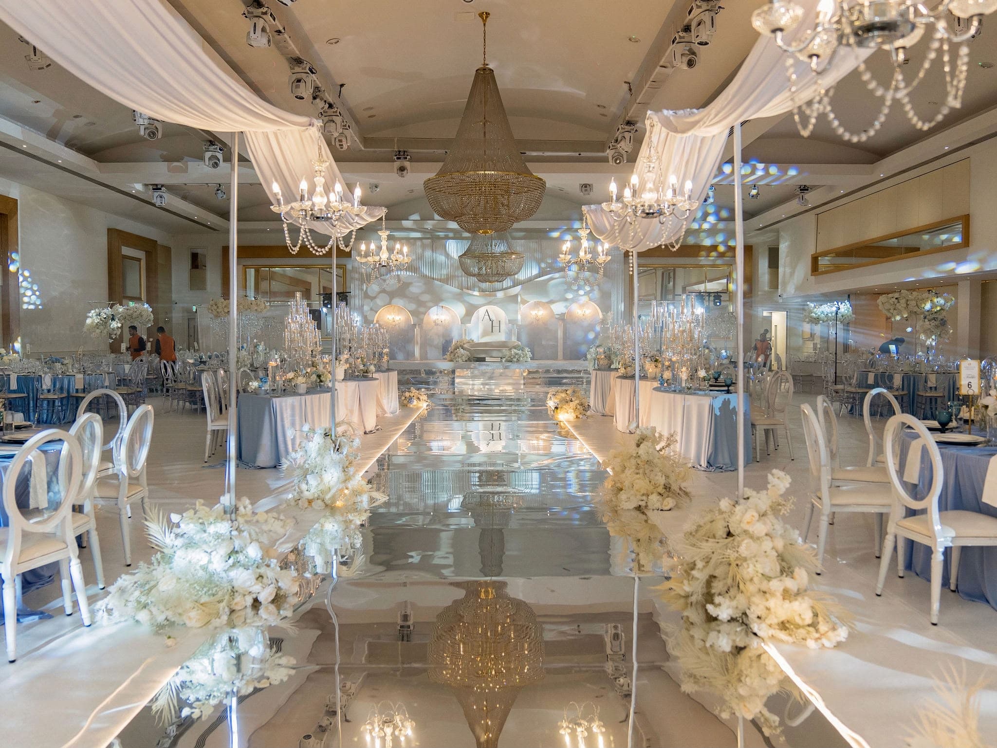 Wide view of a blue and white reception with chandeliers and mirrored dance floor
